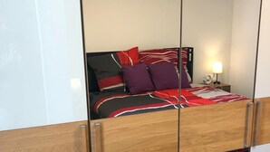 A bedroom with a bed, a nightstand, a lamp, and a mirror. - 2 room apartment with terrace (Roth-sur-Our)
