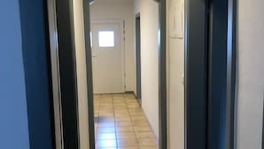 A hallway with a tiled floor, white walls, and dark-colored doors. - 2 room apartment with terrace (Roth-sur-Our)
