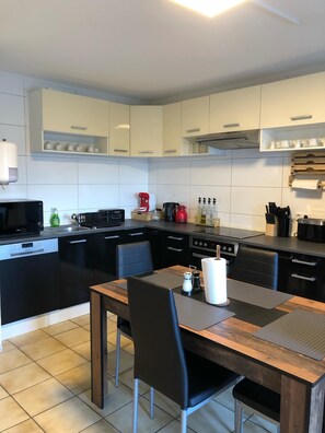 Cozinha moderna com armários brancos, bancada preta e mesa de jantar de madeira com cadeiras.