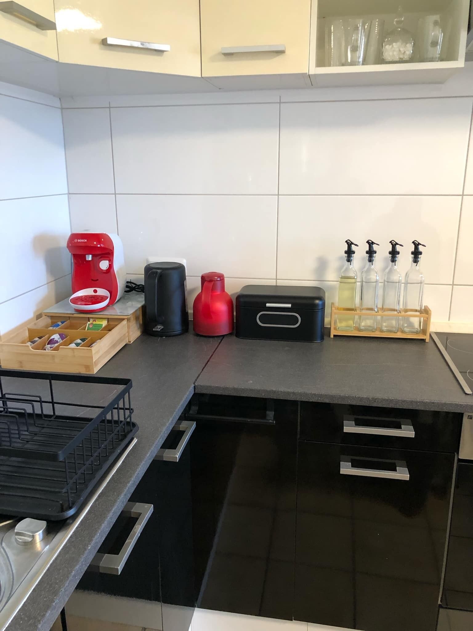 Eine Küche mit einer Bosch-Kaffeemaschine, einer roten Wasserflasche, einem schwarzen Thermosbehälter und einem Set aus Glasflaschen mit Dosierern.