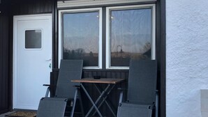 A patio with two folding chairs and a table, a white door, and a window with a view of the landscape. - 2 room apartment with terrace (Roth-sur-Our)