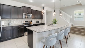 A modern kitchen with dark cabinets, a granite countertop, stainless steel appliances, and pendant lighting. - 5BR Poolside Retreat (Kissimmee)