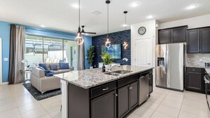 A modern kitchen with dark cabinetry, a stainless steel refrigerator, and a granite countertop. - 5BR Poolside Retreat (Kissimmee)
