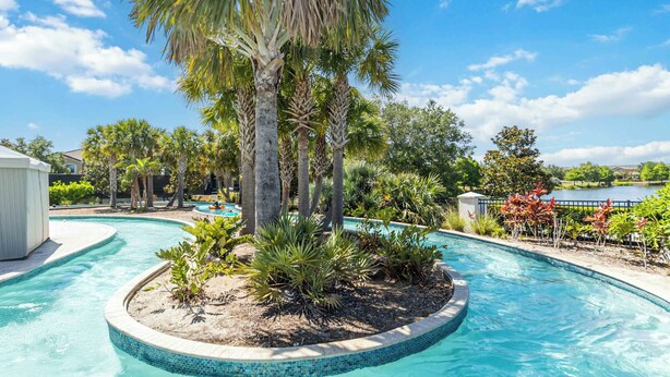 A swimming pool with a circular island surrounded by palm trees and tropical plants. - 5BR Poolside Retreat (Kissimmee)