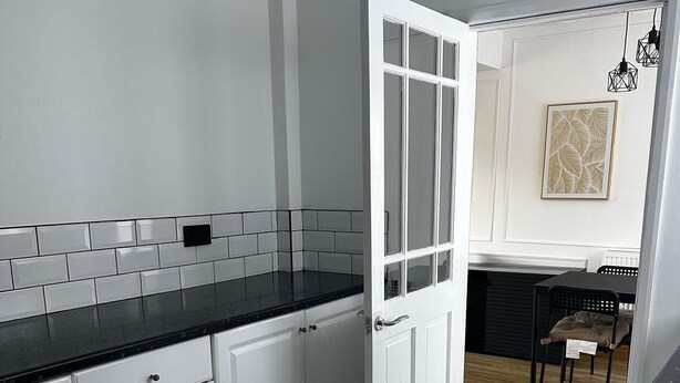 Een moderne keuken met witte kasten, zwarte aanrechtbladen en een betegelde achterwand.