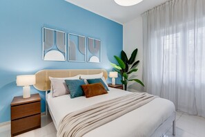 Un dormitorio con una cama, mesitas de noche, decoración en la pared y una planta.