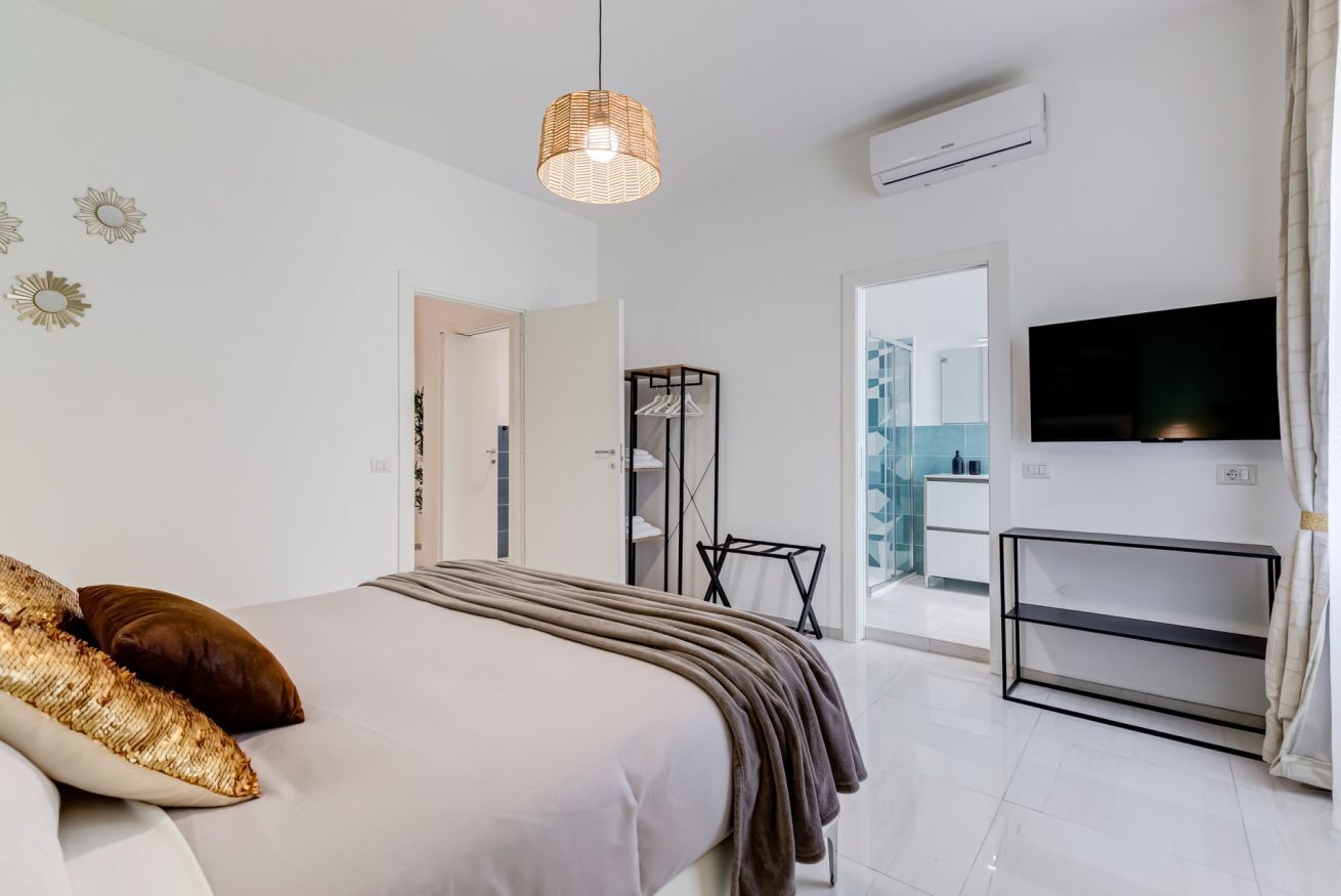 A modern bedroom with a bed, a TV, and a view of a bathroom.