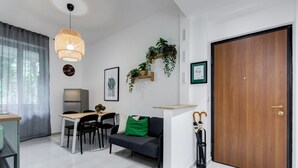 A modern living room with a dining area, a sofa with a green pillow, a wooden door, and a hanging plant. - BDC - Green Nrg! 2-BDR free parking (Rome)