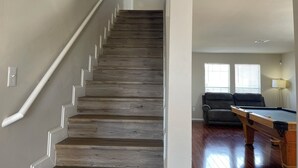 A staircase with wooden steps and white handrails, leading to a living area with a pool table and a couch.