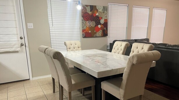 A dining area with a marble table and cushioned chairs, a sofa, and a colorful abstract painting on the wall.