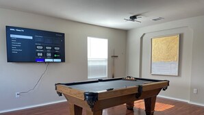 A pool table in a room with a mounted TV displaying a Roku interface.