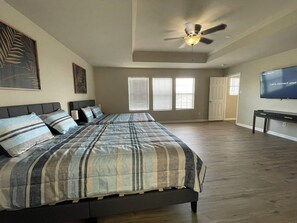 Une chambre spacieuse avec un grand lit, un ventilateur de plafond et un téléviseur fixé au mur.