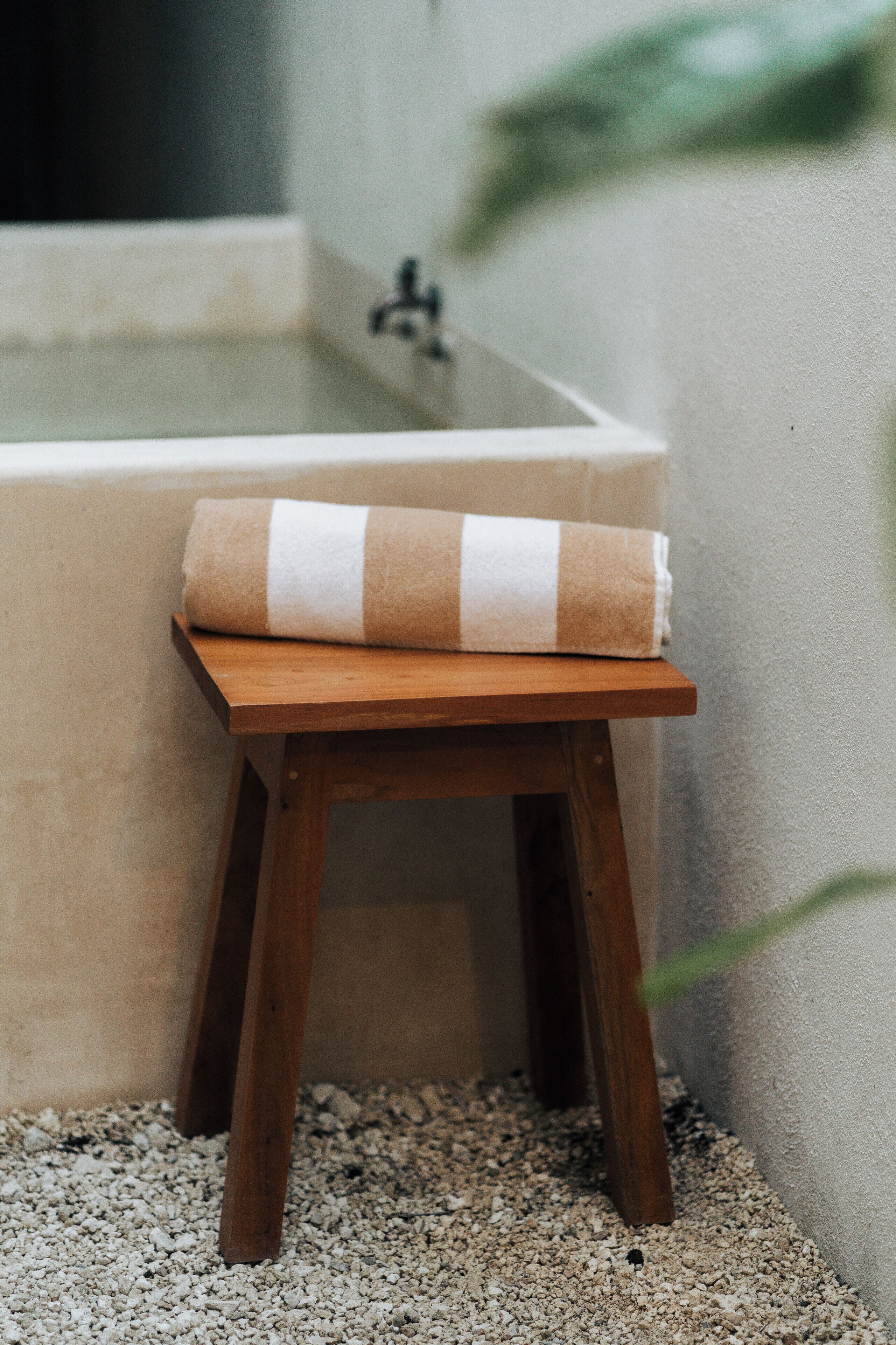 A small wooden stool with a towel placed on top, positioned next to a bathtub.