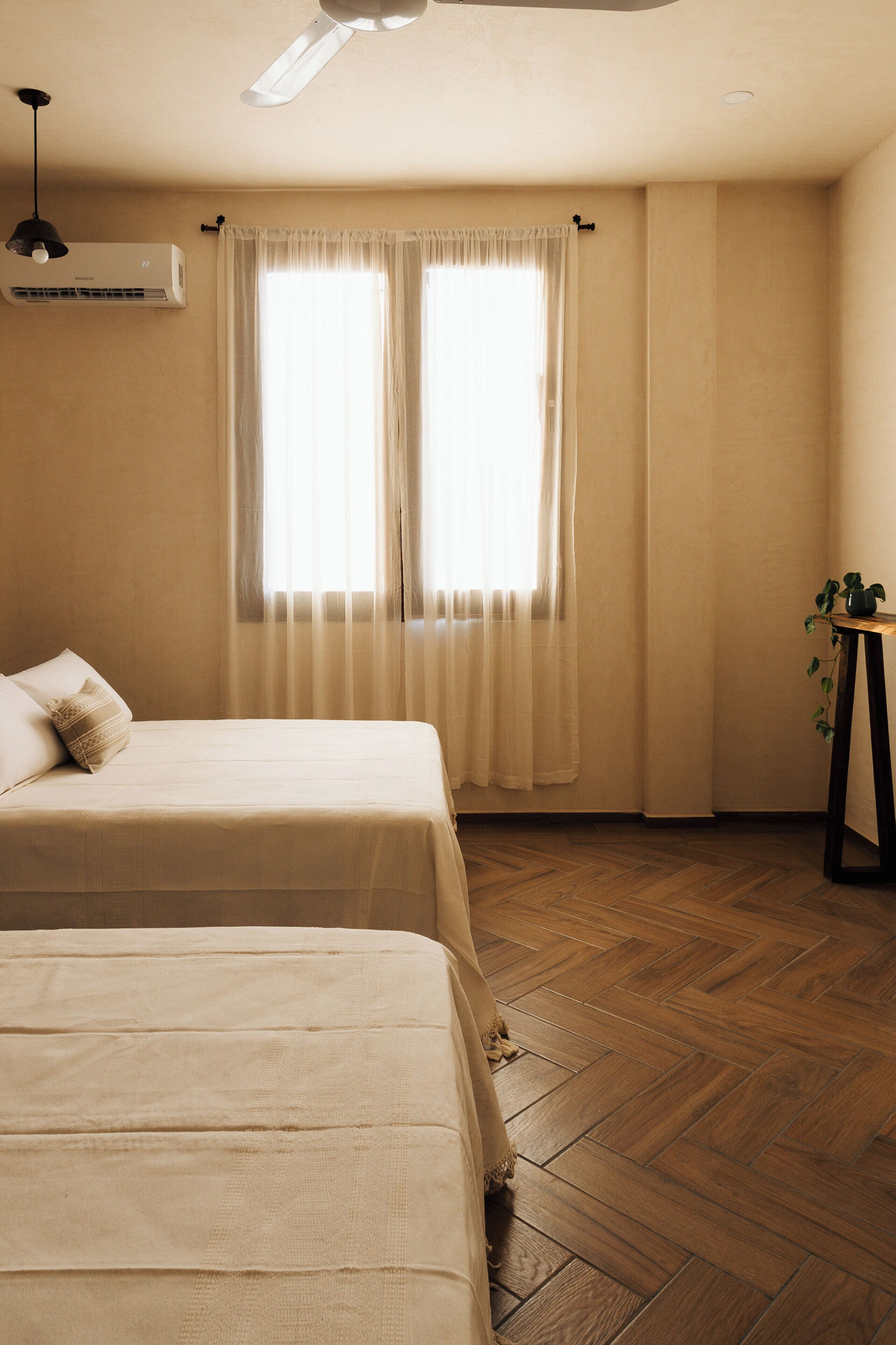 Una habitación con dos camas, ventilador de techo, aire acondicionado y piso de madera.
