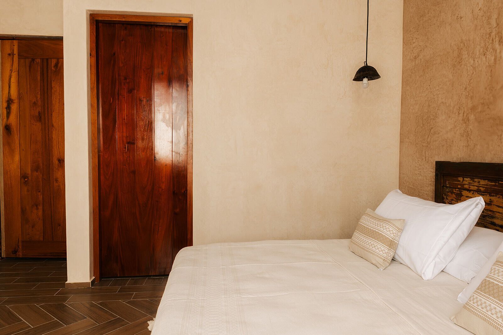 A bedroom with a wooden door, a bed with white bedding, and a hanging light fixture.