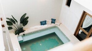 A small, modern bathroom with a corner bathtub, a potted plant, and a window with curtains. - Casa Hotel Izkina (Cozumel)