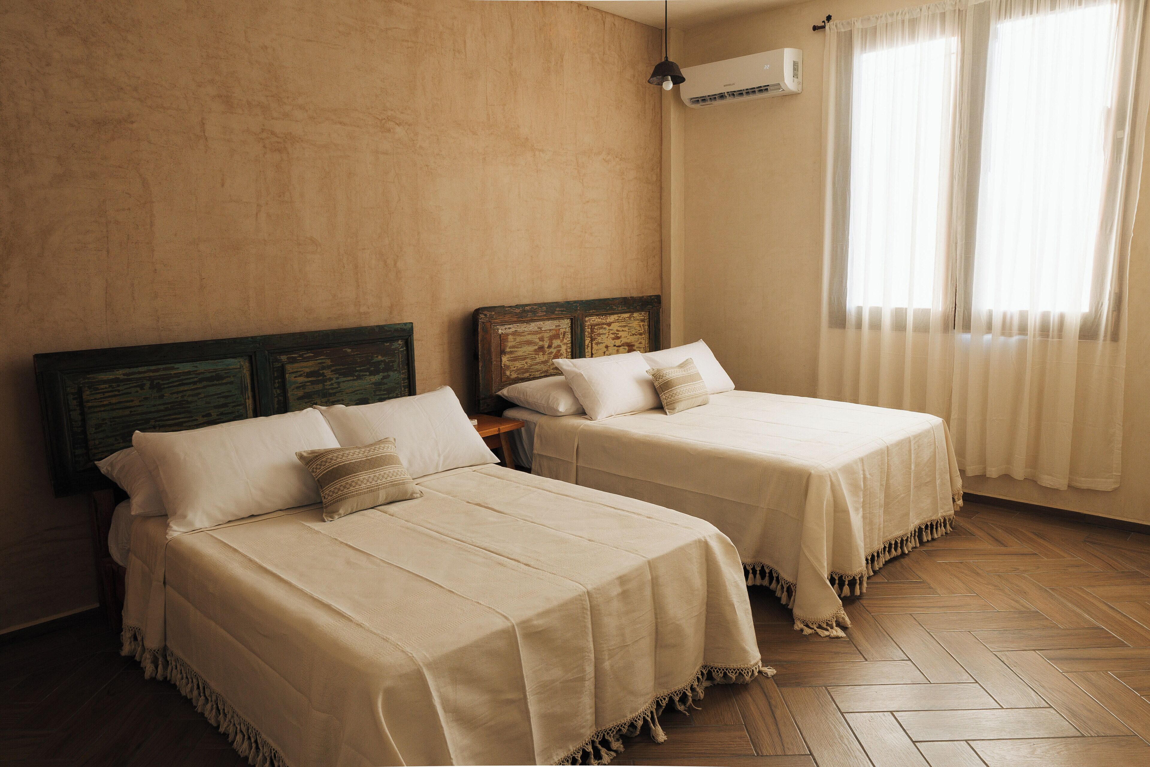 Two beds with wooden headboards, a wooden floor, and a window with curtains.