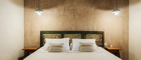 Una cama con cabecera de madera, dos mesitas de noche y dos lámparas colgantes.