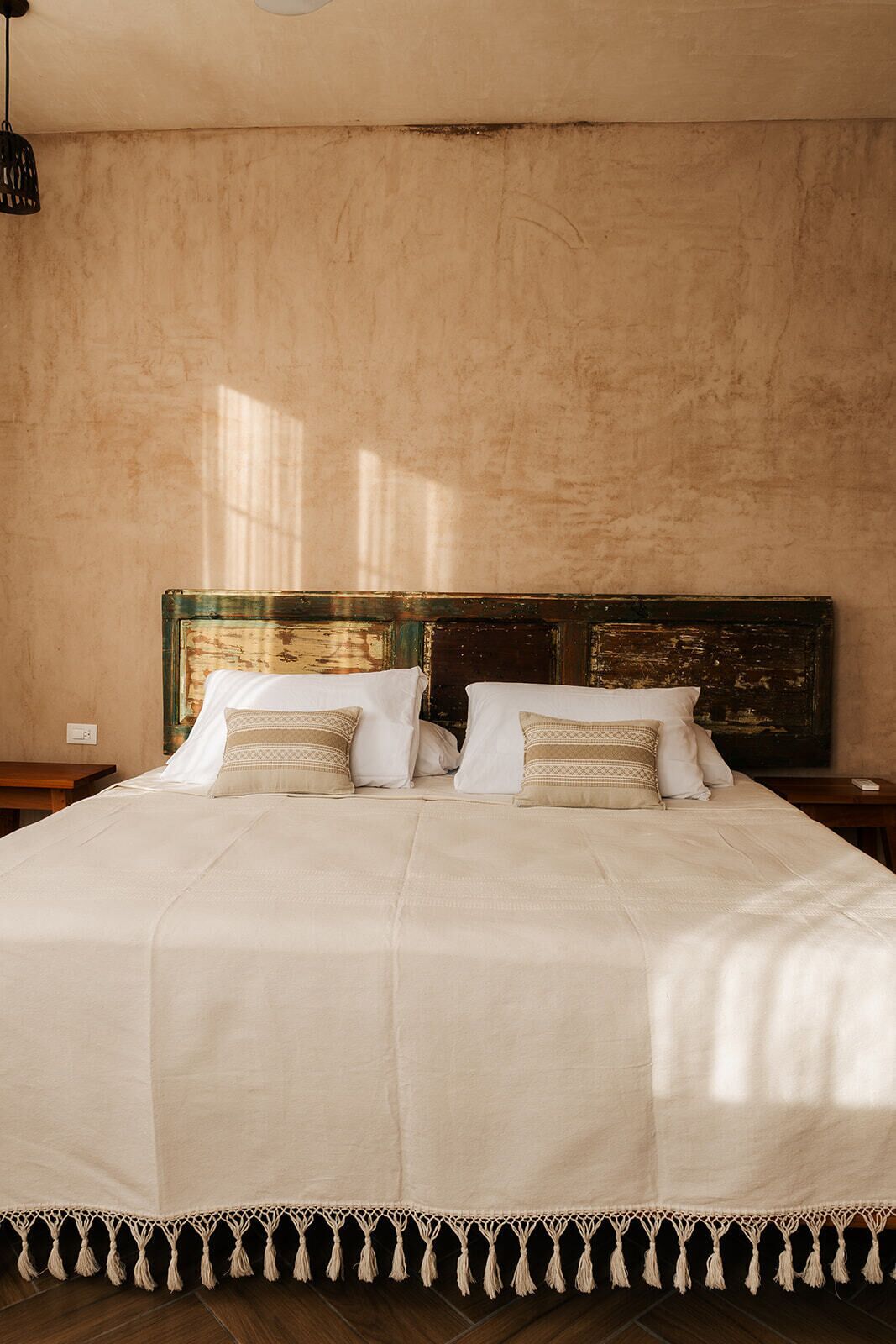 A large bed with a white bedspread and matching pillows, a wooden headboard, and a macramé border.