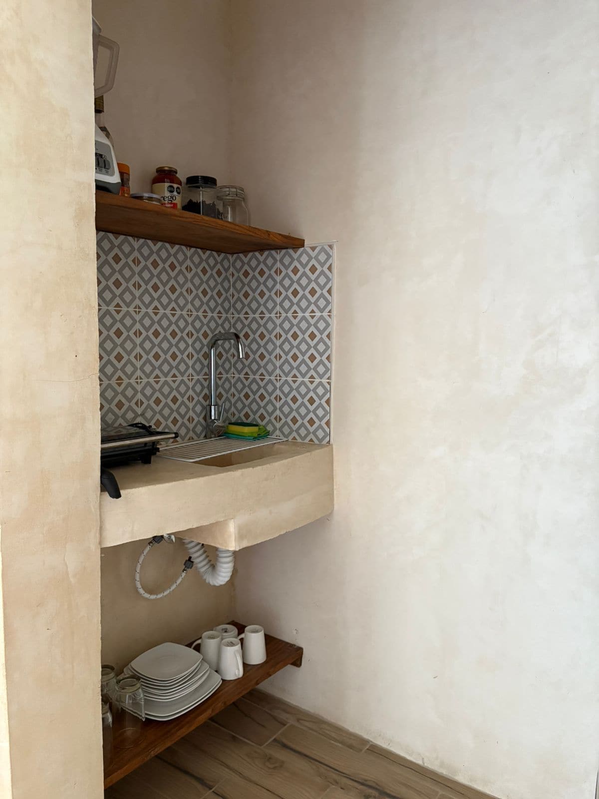 Een kleine keuken met een ingebouwd spoelbakje, een decoratieve spatwand en houten planken boven en onder de spoelbak.