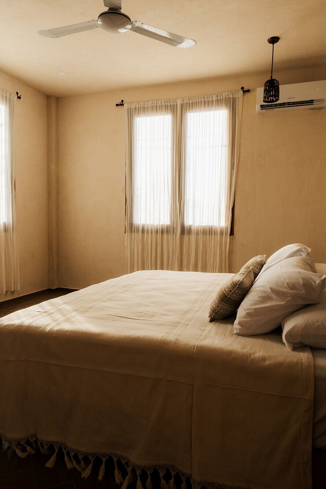 Een slaapkamer met een bed, gordijnen, een plafondventilator en een airconditioning.