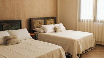 Habitación de hotel con dos camas, ventilador de techo, unidad de aire acondicionado y una ventana con cortinas.