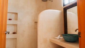 Un baño con ducha, un lavabo y estantes con recipientes pequeños.