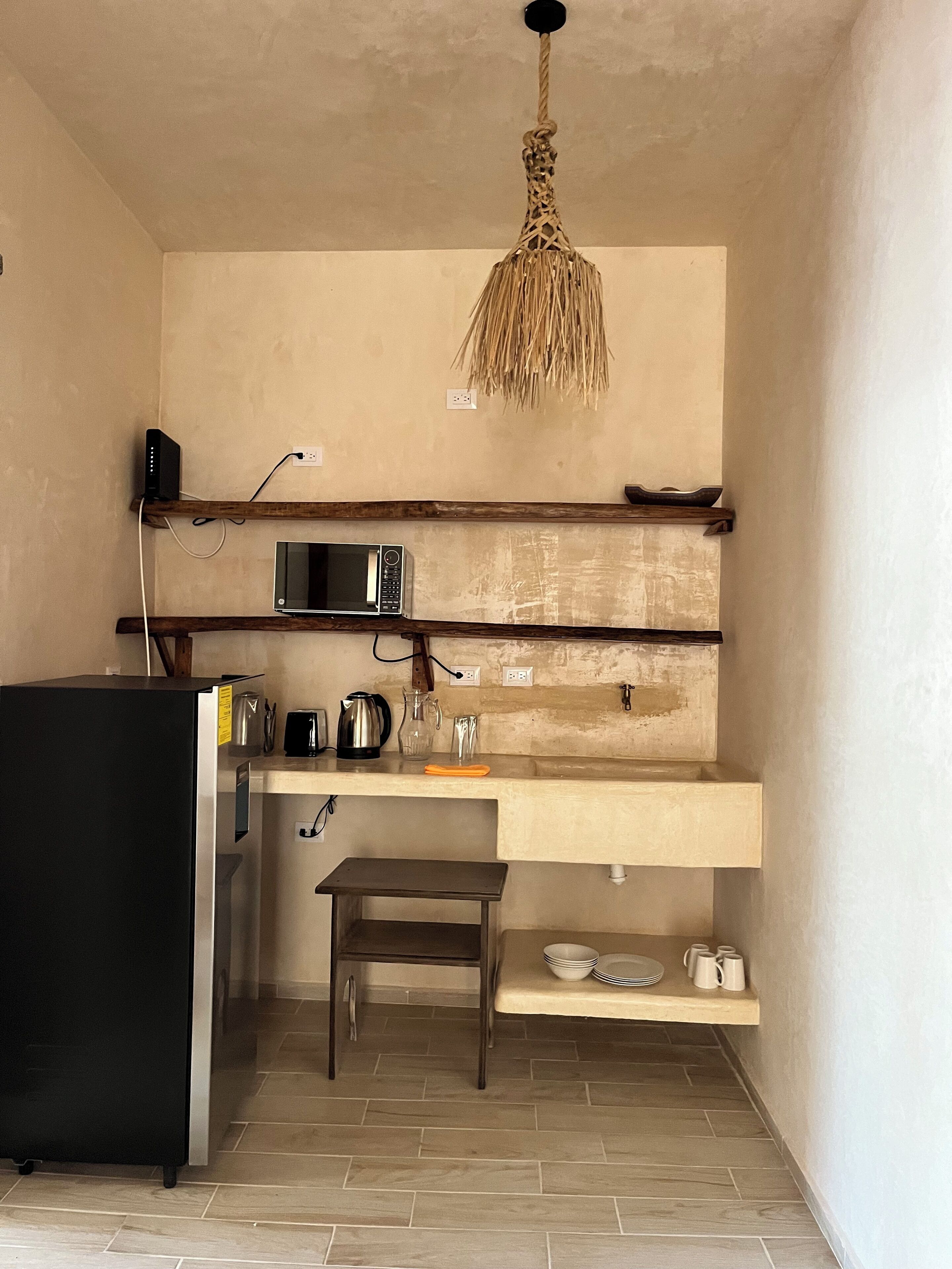 A compact kitchen with a microwave, kettle, and coffee maker on the counter, a small table, and a hanging light fixture.