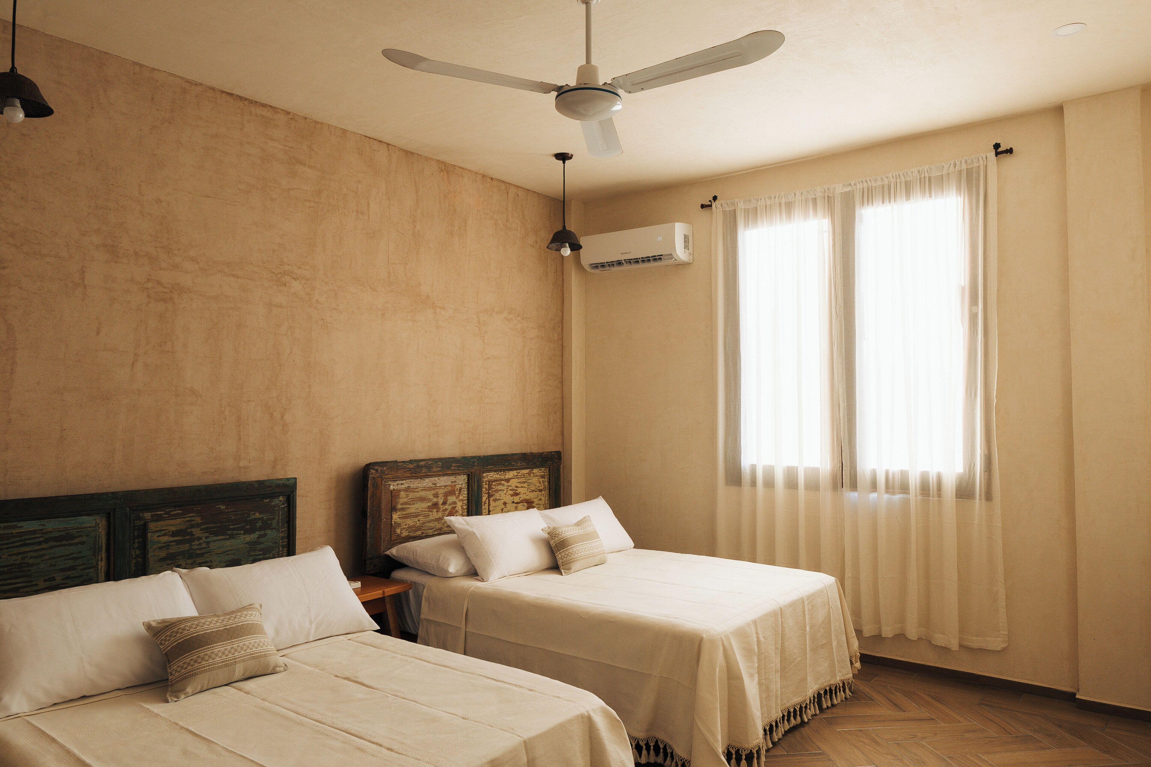 A bedroom with two beds, a ceiling fan, an air conditioning unit, and a window with curtains.