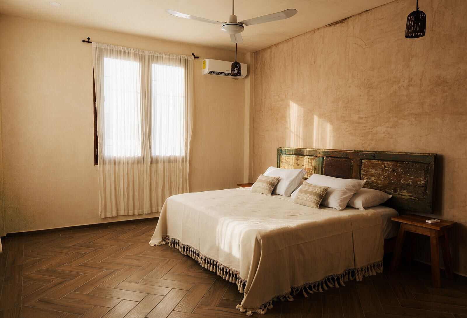 A bedroom with a large bed, wooden floor, ceiling fan, and a window with curtains.