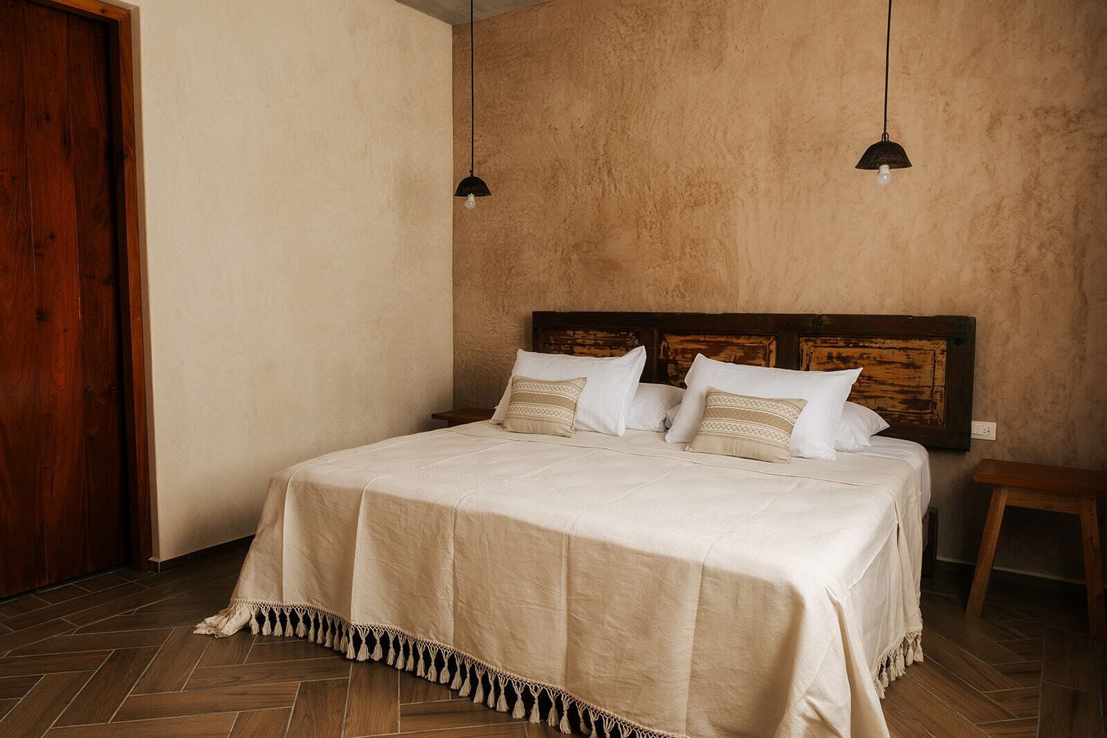 Une chambre avec une tête de lit en bois, un lit avec une literie blanche, deux lampes suspendues et un plancher en bois.