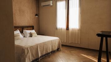 A bedroom with a bed, a nightstand, a desk, and an air conditioning unit.