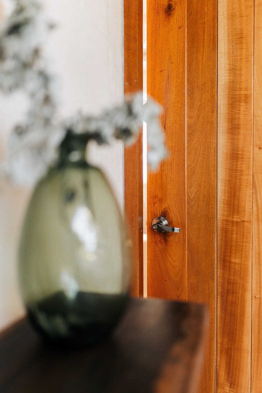 A wooden door with a silver handle and a glass vase with flowers on a dark surface.