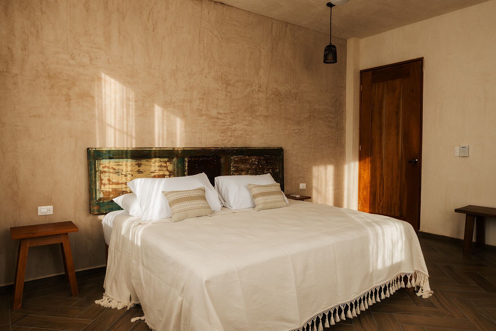 A bedroom with a large bed, a wooden headboard, a small bedside table, and a wooden door.