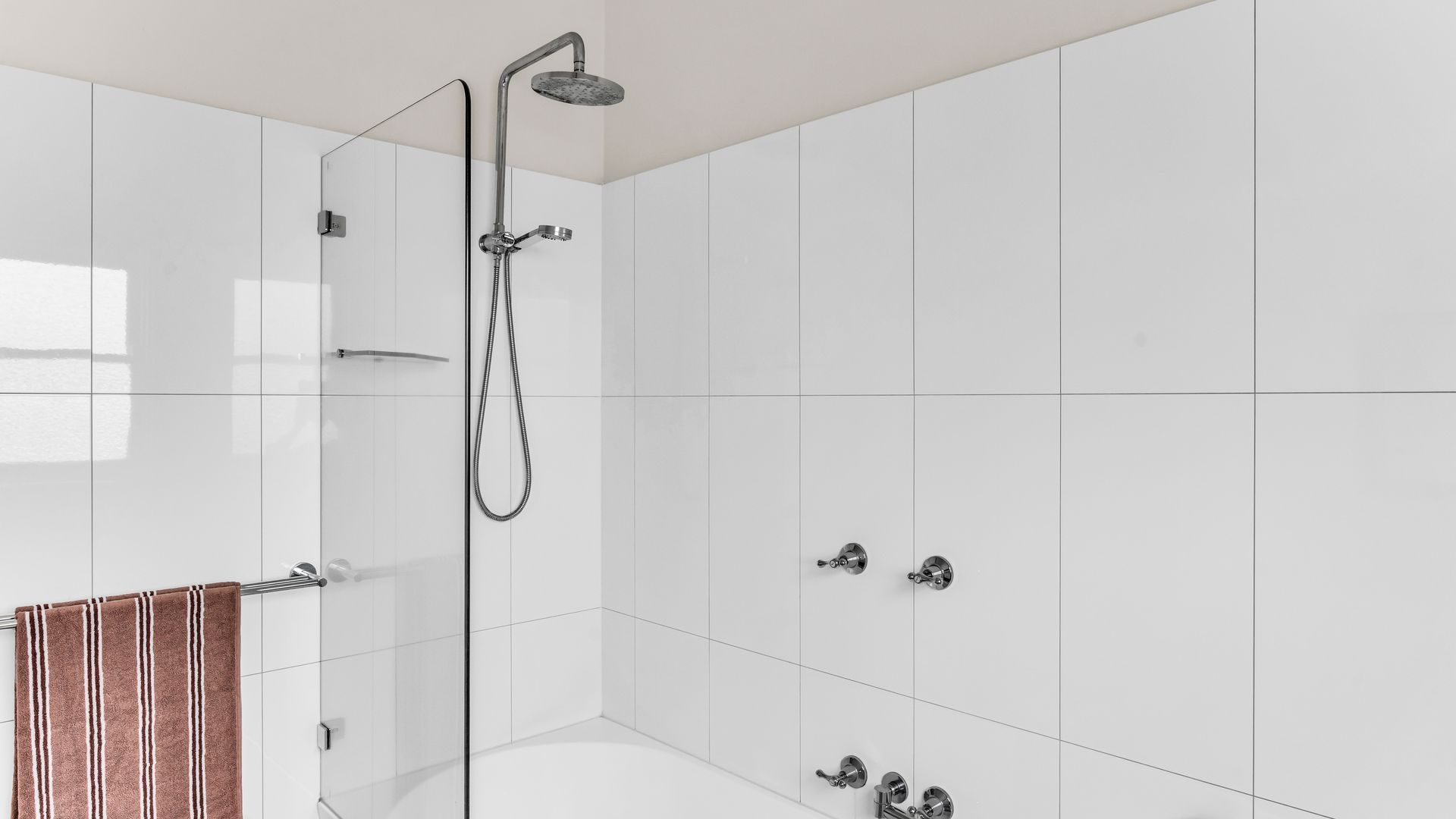 A modern bathroom with a glass shower enclosure, a white bathtub, and a towel rack with a striped towel.