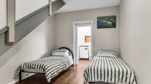 A small room with two single beds, a wooden floor, a white door, and a painting on the wall.