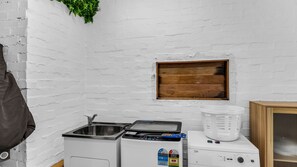 A compact kitchenette with a sink, a small stove, and a washing machine. - Blue Pacific Holiday Home - Murrah St 73 (Bermagui)