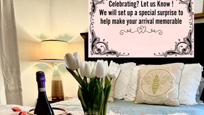 A bed with white bedding, a bottle, a vase with flowers, candles, and scattered rose petals.