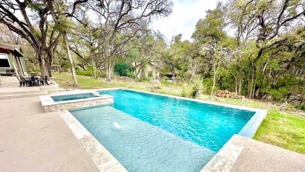 A rectangular swimming pool with a stone border, surrounded by a grassy area and trees.