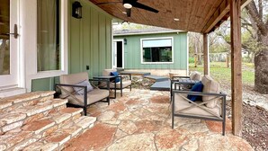A covered patio area with stone flooring, outdoor furniture, and a ceiling fan.