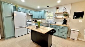 A modern kitchen with light blue cabinets, a central island, and a stainless steel refrigerator.