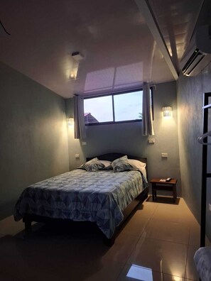 Une chambre à coucher comprenant un lit, une table de chevet, une fenêtre et un appareil de climatisation.
