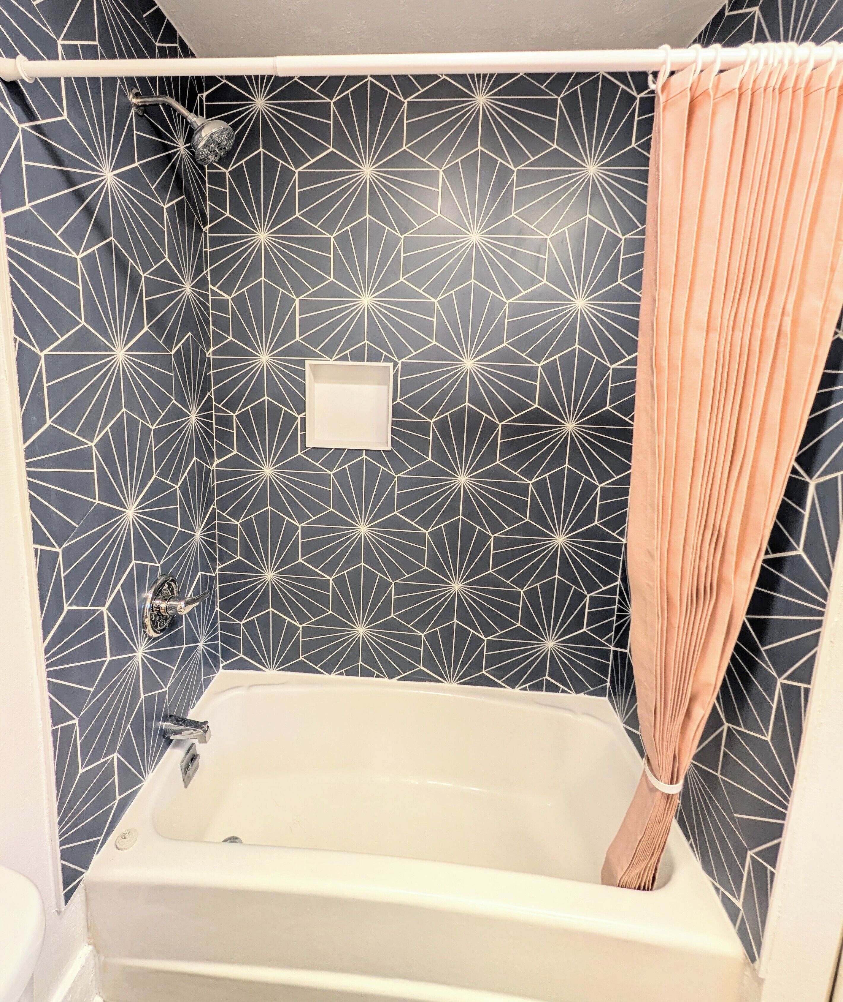 A bathroom with a geometric patterned wall, a white bathtub, and a peach-colored shower curtain.