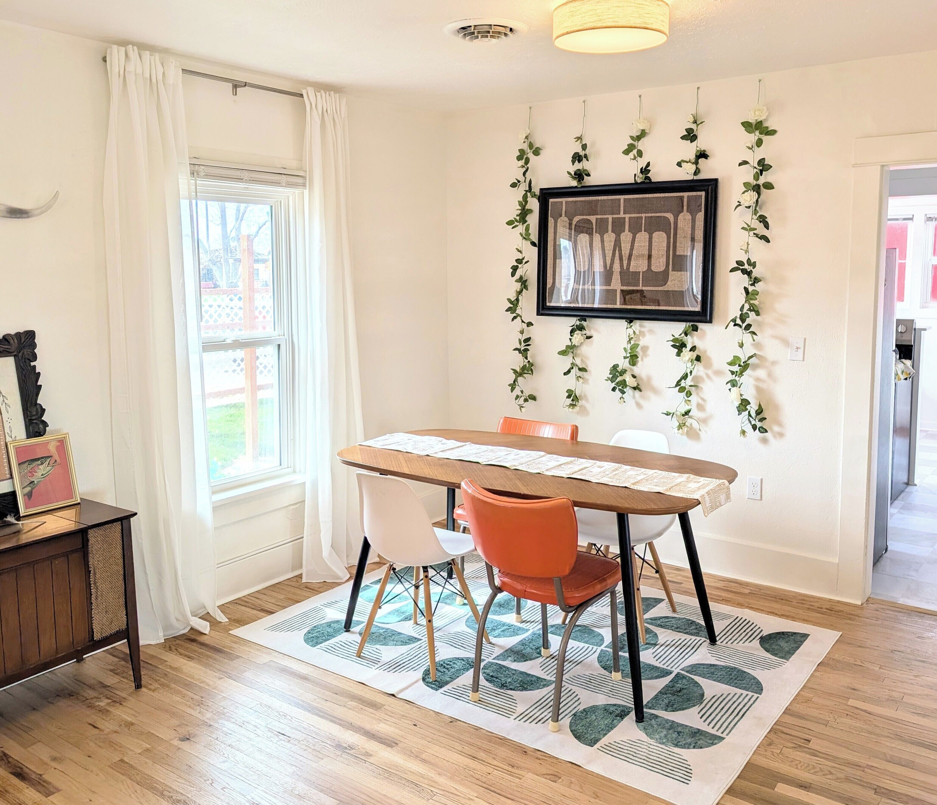 Un coin repas comprenant une table en bois, deux chaises, un tapis et un cadre photo fixé au mur.