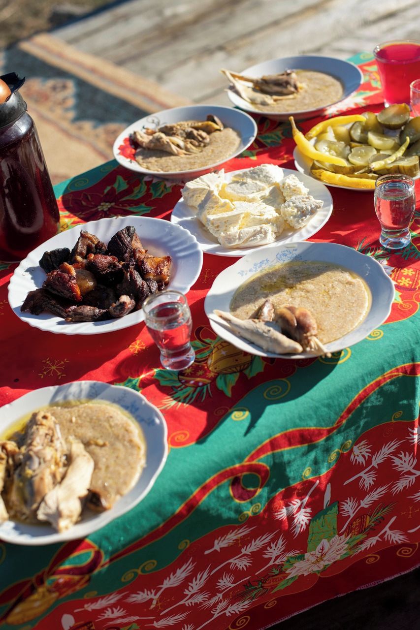 Una mesa con diversos platos, incluyendo carne, verduras y un tazón de sopa, sobre un mantel colorido.