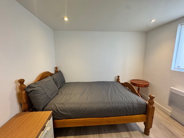 A bedroom with a wooden bed, grey bedding, a small wooden nightstand, and a round table.