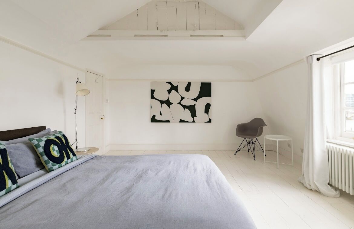 Un dormitorio con cama, una silla, una mesita y un cuadro abstracto grande en la pared.