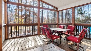 Un espace extérieur aménagé, abrité et doté d’une table et de chaises, de grandes fenêtres et d’une vue sur les arbres.
