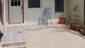 Un edificio pequeño de una sola planta con entrada de baldosas, una silla azul y plantas en macetas.
