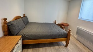 A neatly made bed in a small, well-lit room with a wooden headboard, a small round table, and a window with blinds. - Two Top Floor Double Rooms (Belvedere)